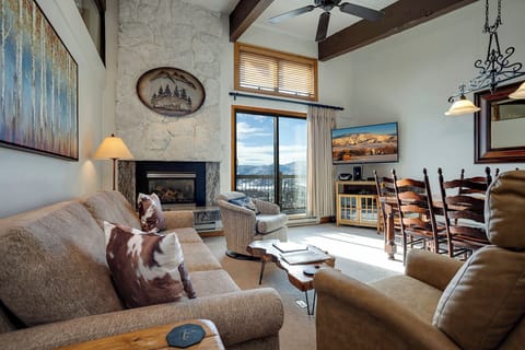 Unwind by your stone fireplace while soaking in stunning mountain views through floor-to-ceiling windows in this cozy yet elegant living space.