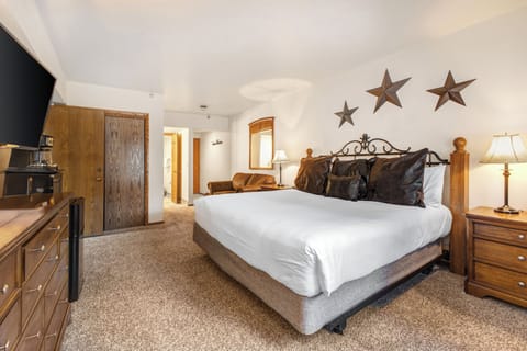 The main suite bedroom has a king size bed, white linens, wooden closet doors and love seat.