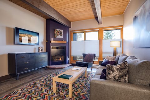 Cozy up by the crackling fireplace in this stylish living room, where warm wood beams and plush seating create your perfect mountain retreat.