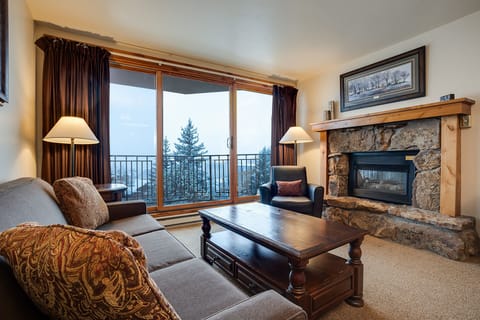Cozy up by your stone fireplace while enjoying mountain views through floor-to-ceiling windows in this warm, inviting living space.