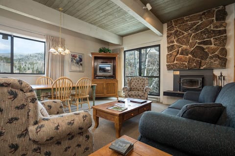 Cozy up in this warm living space with rustic stone fireplace, comfortable seating, and mountain views through large windows.