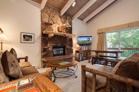 Unwind in your cozy living room featuring a stunning stone fireplace, rustic wood beams, and comfortable seating perfect for mountain evenings.