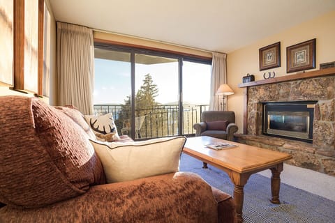 Curl up by your cozy stone fireplace while enjoying mountain views through floor-to-ceiling windows in this warm, inviting living space.