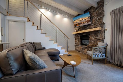 Unwind in your stylish living room featuring a cozy stone fireplace, modern sectional, and warm lighting for perfect mountain evenings.