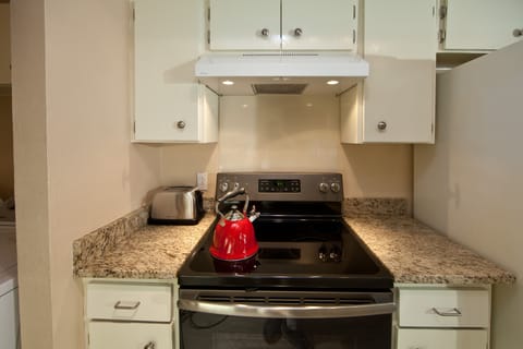 Electric range with whistling kettle and essential kitchen supplies in cabinets