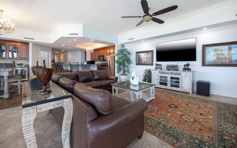 This living area features a cozy brown leather sofa, a large TV, and a stylish coffee table on a vibrant area rug