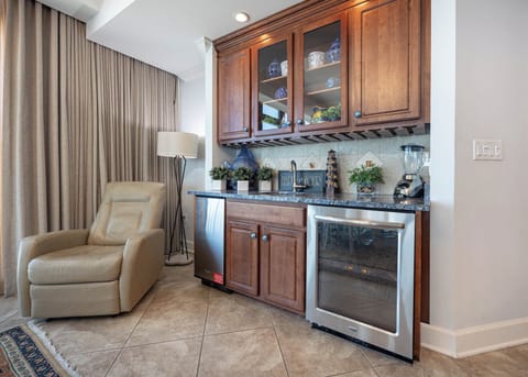 This inviting wet bar features rich wooden cabinetry, a wine cooler, and a cozy chair for relaxation