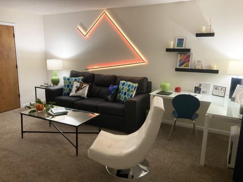 A white swivel chair faces a metal-framed glass coffee table, with wall shelves displaying photos and candles.