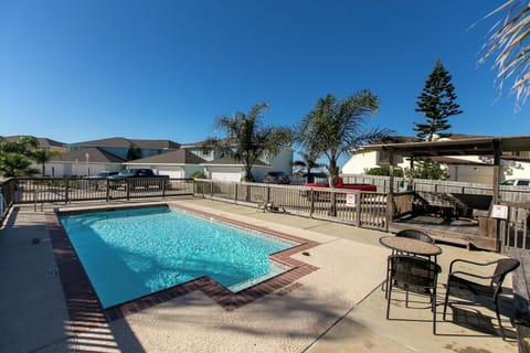 Pool area surrounded by palm trees and residential buildings with outdoor seating and clear blue skies overhead.