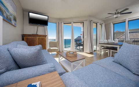 Bright living area with a striped sofa with queen sleeper, flat-screen TV, and sliding balcony doors with a beach front view