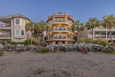 Multi-story beachfront property at dusk with rock jetty