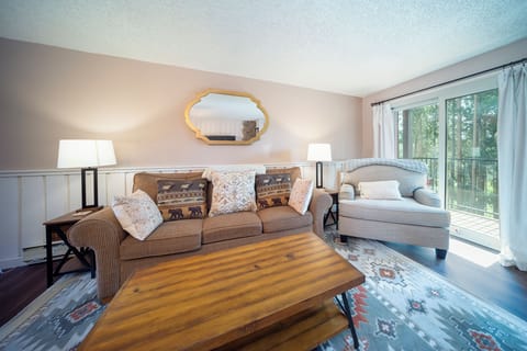 Unwind in your cozy living room featuring plush seating, warm natural light, and peaceful views of the surrounding greenery through expansive windows.