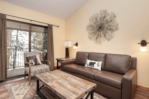 Unwind in your stylish living space with cozy leather seating, rustic wood accents, and forest views from your private balcony.