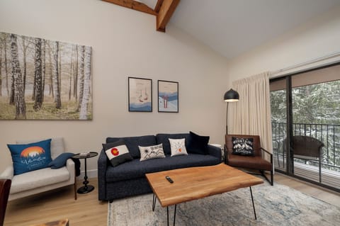 Unwind in your cozy living room with rustic beams overhead, surrounded by mountain-inspired décor and snow-dusted forest views from your private balcony.