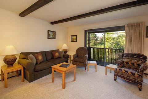Unwind in your cozy living space with exposed beams and balcony views of lush greenery through large windows.