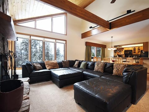 Unwind in your spacious living room with plush leather seating, soaring ceilings, and stunning forest views through expansive windows.