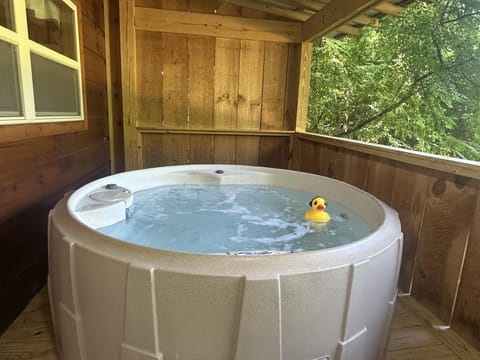 Bubbling round hot tub with a yellow rubber duck, surrounded by natural wood walls and leafy green views.