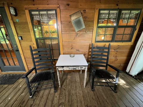 Wood-paneled porch with two black ladder-back rocking chairs and a distressed white side table.