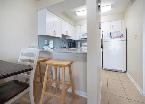 This kitchen features sleek white cabinetry, granite countertops, and a cozy dining area with bar stools for casual meals