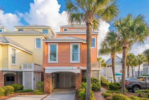 Vibrant coral-colored coastal home with tropical palm trees and covered parking creates your perfect beach getaway entrance.