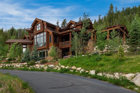 Mountain lodge architecture nestled among towering evergreens with natural stone landscaping and private driveway access.