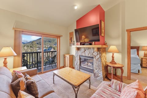 Unwind in your cozy mountain retreat with a stone fireplace, balcony views, and comfortable seating for perfect relaxation.