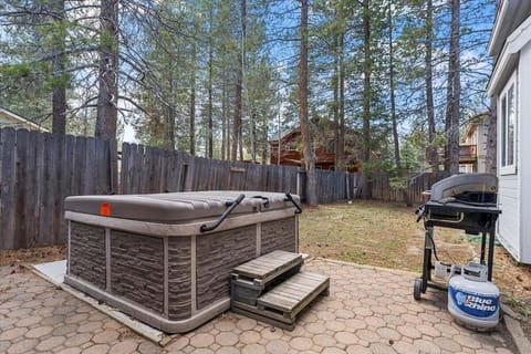 Patio with hot tub, hot tub cover, steps, grill, fence, trees, and yard.