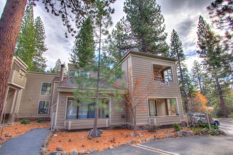 Multi-level exterior with entry door, house number, windows, upper balcony, walkway, parking area, and trees.