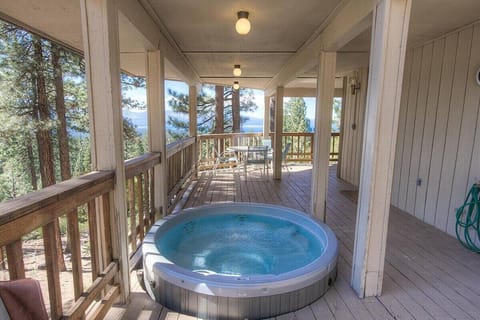 Covered deck with hot tub, patio table for four, railing, lake view, mountains, and trees.
