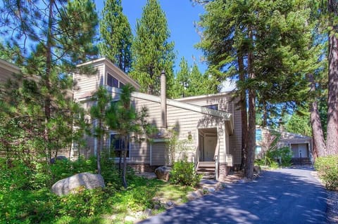 Multi-level exterior with covered entry, exterior stairs, driveway, house number sign, windows, chimney, trees, and boulders.