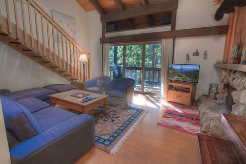 Living room with sectional sofa, armchairs, coffee table, TV, fireplace, sliding door, deck, staircase, and loft railing.