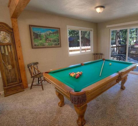 Pool table with cue sticks, billiard balls, windows, and patio seating visible beyond the slider.