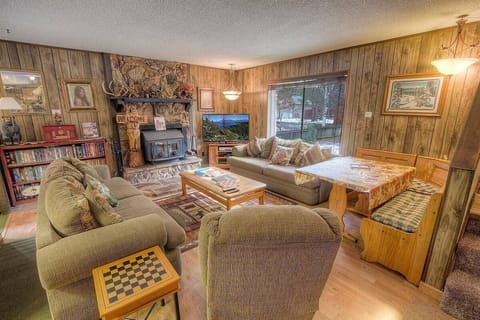 Living room with fireplace, flat-screen TV, sofa seating, armchair, large window, bookshelf, and dining nook.