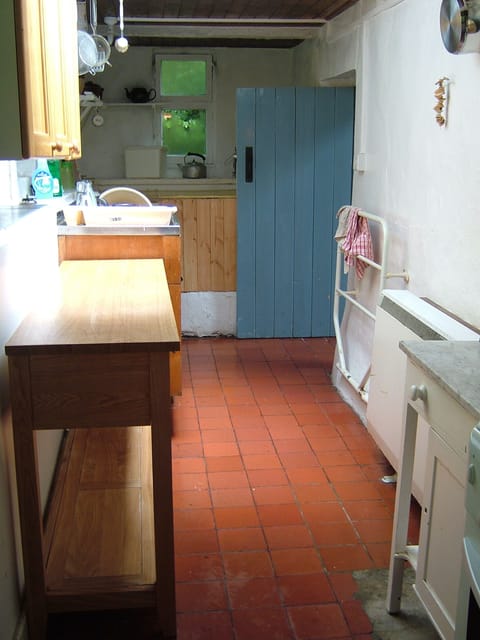 The kitchen, with tile floor - worksurfaces and sink. Cooker and fridge behind