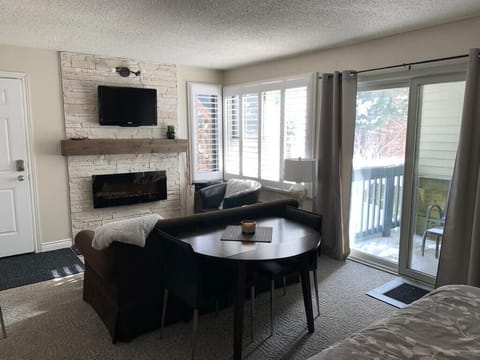 Main living area with electric fireplace and hillside view with evergreen trees!