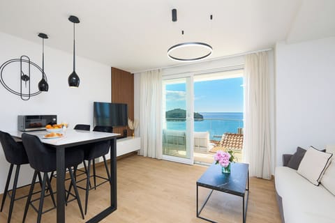 The bright, open-plan living area is styled with modern black accents and opens onto a private balcony. From here, you can enjoy stunning, uninterrupted views of the deep blue Adriatic Sea.