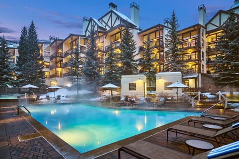 The property stands among snow-dusted evergreens, featuring an inviting heated outdoor pool where steam rises into the evening mountain air—a perfect winter retreat awaits.