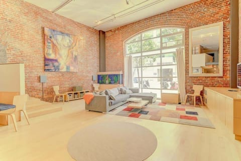 Sun-filled loft with exposed brick, soaring ceilings, and cozy modern furnishings—an inviting retreat blending warmth, style, and urban charm.