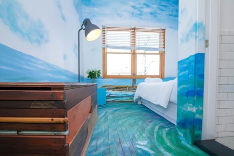 Art-filled bedroom with ocean-inspired mural, unique flooring, and cozy bed—bright, creative, and one-of-a-kind coastal retreat.
