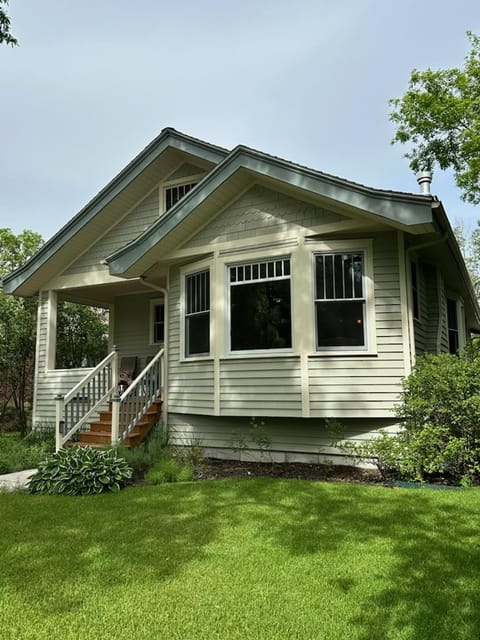 Grass lawn in front of light gray siding with scalloped trim and white-framed windows under a peaked roofline.