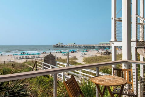 Your private balcony overlooks soft sand, turquoise umbrellas, and a charming pier stretching into the calm sea—the perfect spot to sip your morning coffee or unwind as gentle waves roll in.