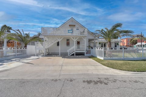 Charming white beach house with wraparound porches, palm trees, and private parking in a tropical coastal setting.