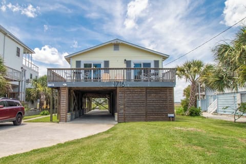Elevated coastal property with covered parking and a welcoming front deck, surrounded by palm trees and neighboring homes in a peaceful beachside community.