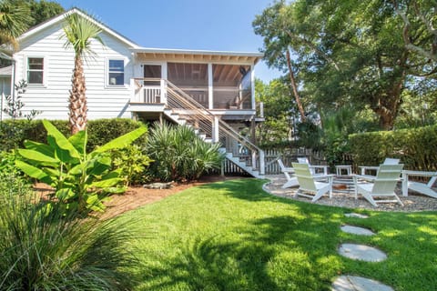 Nestled among mature trees and tropical palms, this charming coastal retreat awaits with a lush lawn and inviting lounge chairs perfect for soaking up the sun.