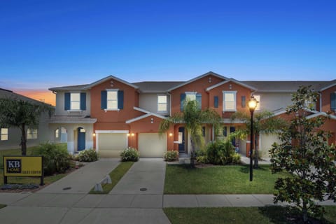 Warm terracotta townhome framed by palms and evening glow, with convenient garage parking-your cheerful home base for Orlando adventures.
