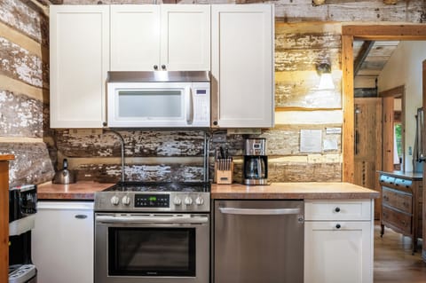 Well-equipped log cabin kitchen with cream cabinetry, stainless steel appliances, and rustic wood walls—perfect for home-cooked meals in a cozy setting.