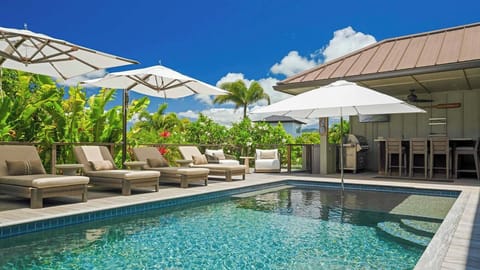 A serene private pool and modern covered bar area surrounded by lush tropical greenery create your perfect outdoor entertaining space under endless blue skies.