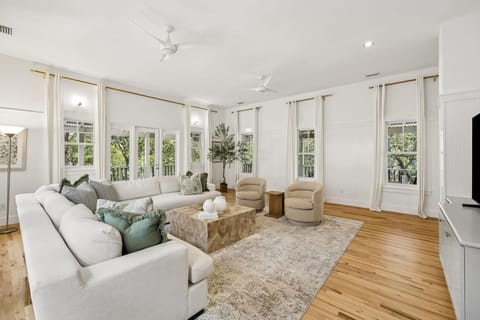 Living room with light hardwood floors, white sectional sofa, swivel chairs, and floor-to-ceiling windows with cream curtains.