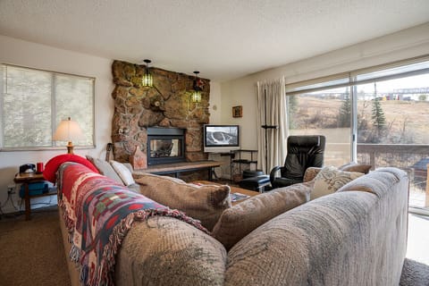 Cozy up in your spacious living room featuring a stunning stone fireplace, plush seating, and panoramic windows showcasing breathtaking mountain views.