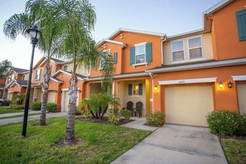 Cheerful orange townhome exterior with palm-lined landscaping and a cozy porch-perfect curb appeal for a sunny Florida stay.